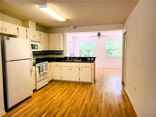 kitchen with dark countertops, a sink, white appliances, a textured ceiling, and light wood-type flooring