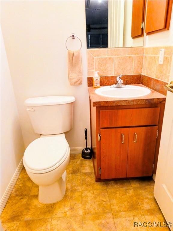 half bathroom featuring vanity, tile patterned flooring, toilet, baseboards, and backsplash