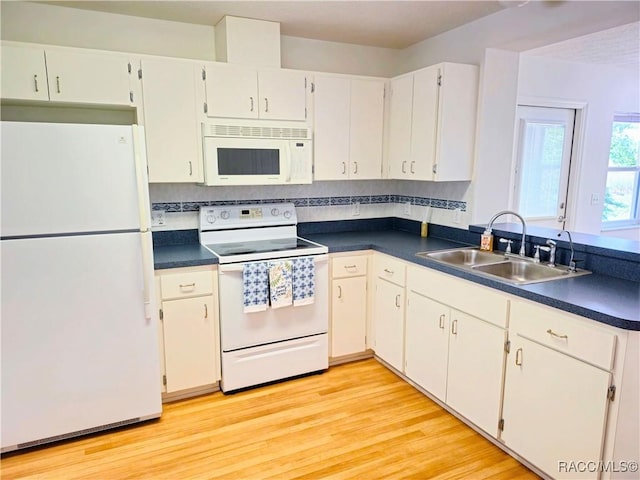 kitchen with a sink, light wood-style flooring, dark countertops, and white appliances