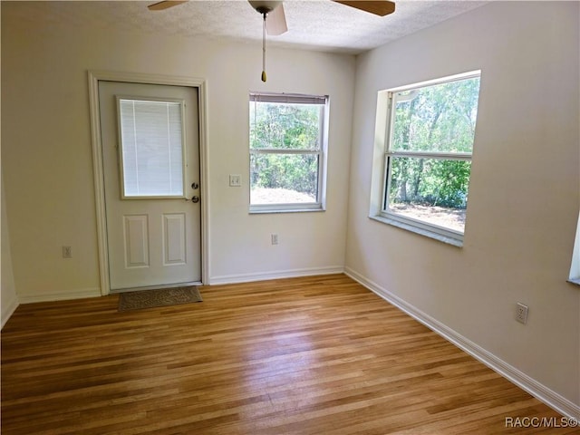 interior space with a textured ceiling, ceiling fan, baseboards, and light wood finished floors