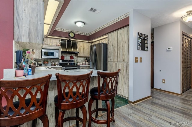 kitchen with light wood finished floors, visible vents, stainless steel appliances, light countertops, and wall chimney range hood