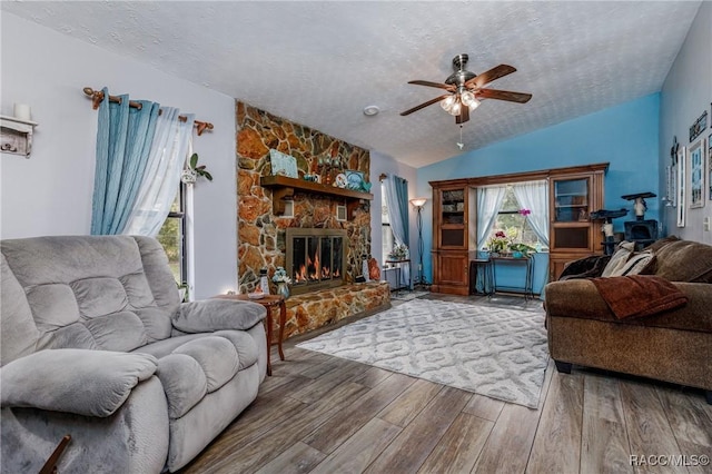 living room with lofted ceiling, a stone fireplace, a textured ceiling, and wood finished floors