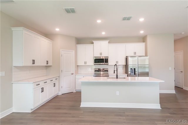 kitchen with appliances with stainless steel finishes, a kitchen island with sink, sink, light hardwood / wood-style floors, and white cabinetry