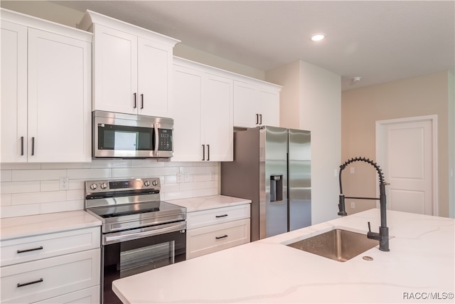 kitchen featuring decorative backsplash, light stone counters, stainless steel appliances, sink, and white cabinets