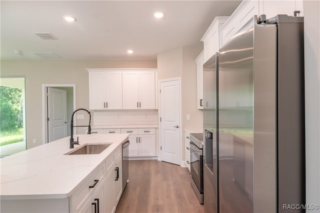 kitchen featuring hardwood / wood-style floors, a kitchen island with sink, sink, white cabinetry, and stainless steel appliances