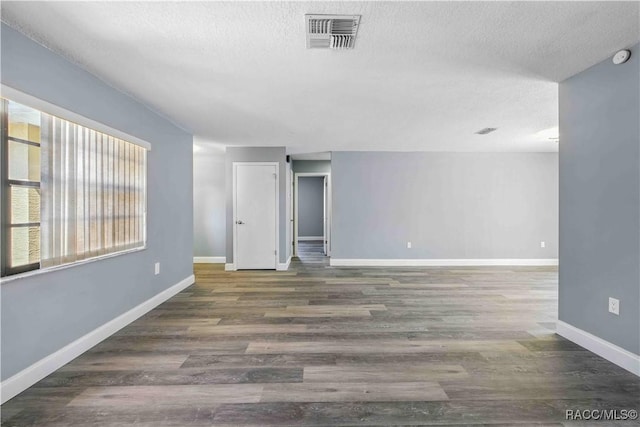 empty room with a textured ceiling, wood finished floors, visible vents, and baseboards