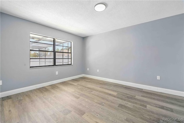 spare room featuring baseboards, wood finished floors, and a textured ceiling