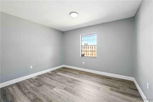 spare room featuring baseboards, wood finished floors, and a textured ceiling