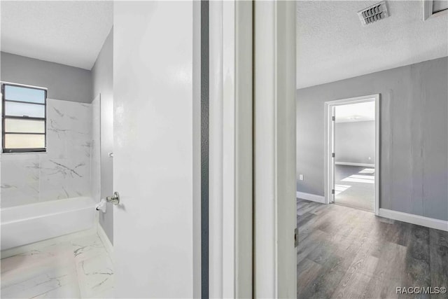full bath featuring wood finished floors, visible vents, shower / bath combination, baseboards, and a textured ceiling