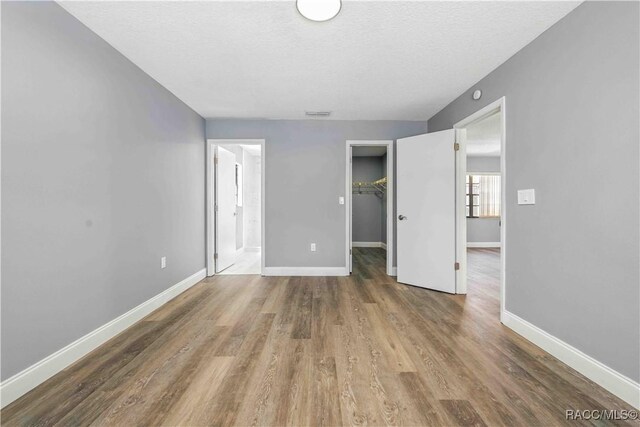 unfurnished bedroom with wood finished floors, connected bathroom, a walk in closet, a closet, and baseboards