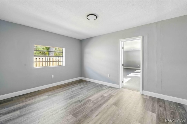 unfurnished bedroom with baseboards, wood finished floors, a textured ceiling, and connected bathroom
