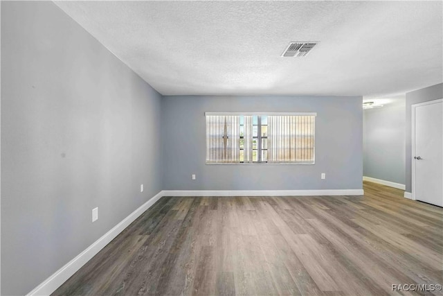 unfurnished room featuring baseboards, wood finished floors, visible vents, and a textured ceiling