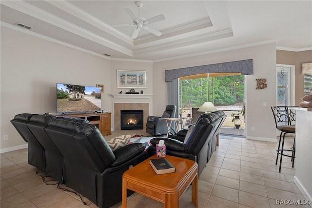 living room with a raised ceiling, light tile patterned flooring, ceiling fan, crown molding, and a tiled fireplace