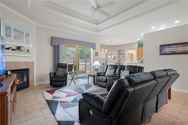 living room featuring ceiling fan, a tile fireplace, light tile patterned flooring, a tray ceiling, and crown molding