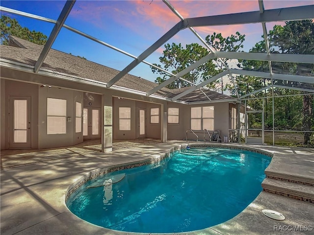 pool at dusk featuring glass enclosure and a patio area