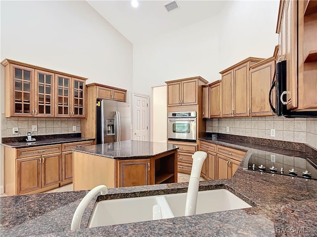 kitchen with a center island, stainless steel appliances, high vaulted ceiling, backsplash, and dark stone countertops