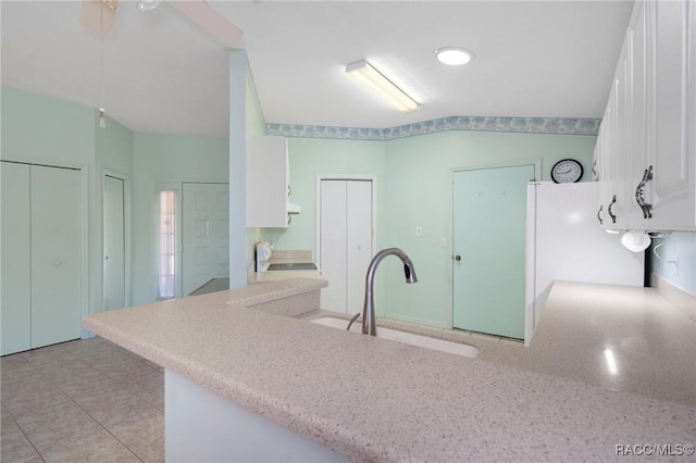 kitchen with white fridge, kitchen peninsula, sink, white cabinets, and range