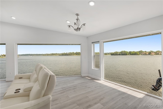 unfurnished room with a water view, an inviting chandelier, lofted ceiling, and light hardwood / wood-style flooring