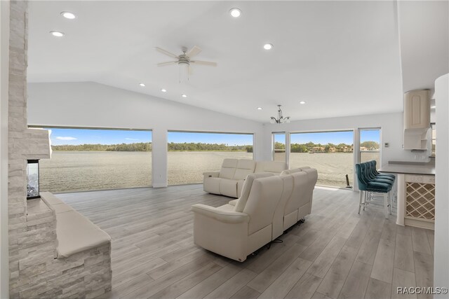 living room with ceiling fan with notable chandelier, lofted ceiling, and light wood-type flooring