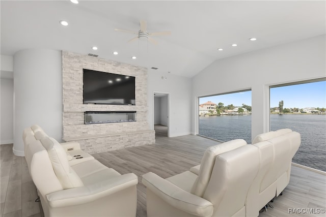 living room featuring lofted ceiling, light hardwood / wood-style flooring, ceiling fan, and a stone fireplace