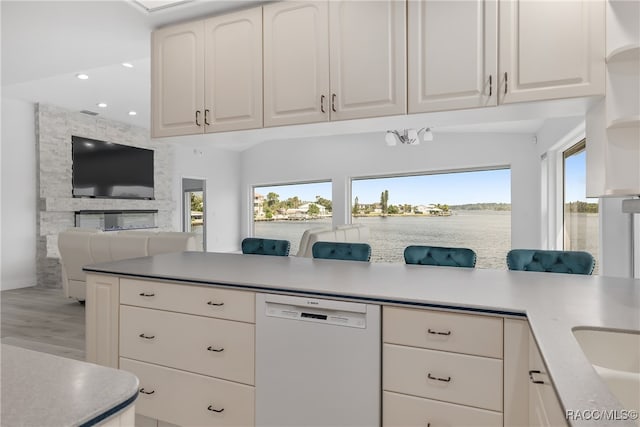 kitchen featuring white dishwasher, a water view, white cabinets, light hardwood / wood-style floors, and a stone fireplace