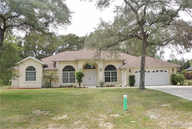 ranch-style home with a front lawn, concrete driveway, an attached garage, a shingled roof, and stucco siding