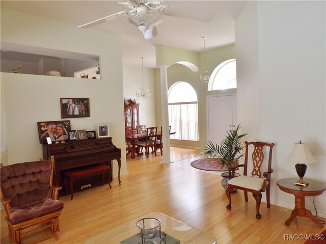 living area featuring ceiling fan with notable chandelier, wood finished floors, and a high ceiling
