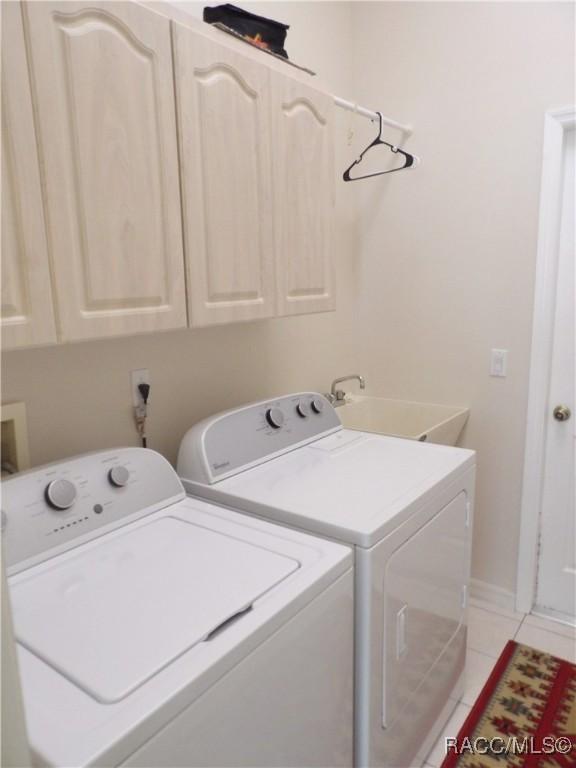 washroom with light tile patterned flooring, washer and dryer, a sink, and cabinet space