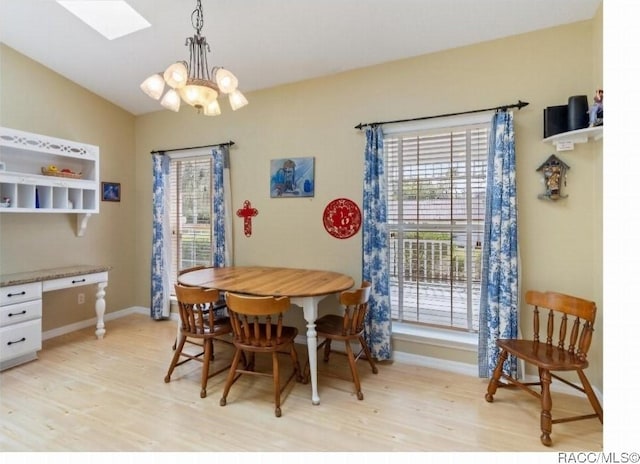 dining area featuring lofted ceiling with skylight, an inviting chandelier, and light hardwood / wood-style flooring