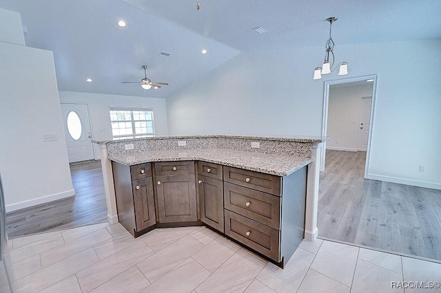 kitchen featuring hanging light fixtures, vaulted ceiling, dark brown cabinets, and light stone counters