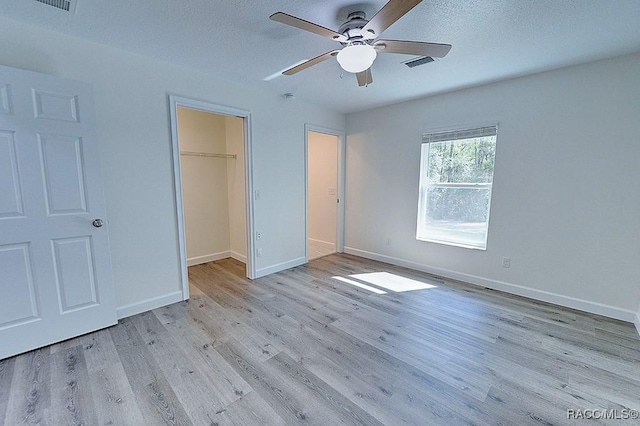 unfurnished bedroom with a closet, a walk in closet, a textured ceiling, and light hardwood / wood-style flooring