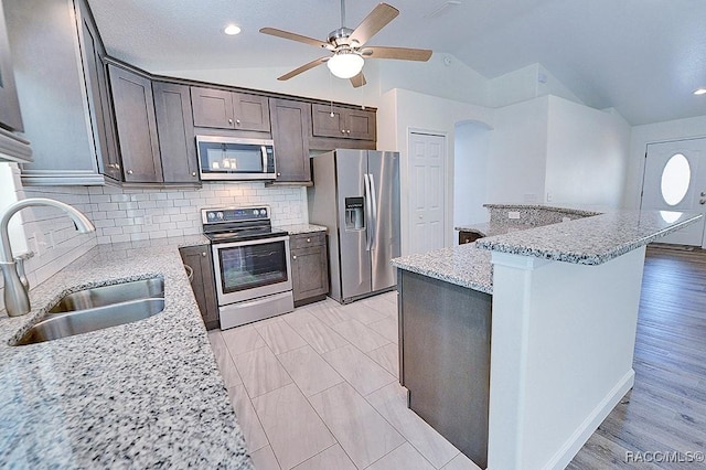 kitchen with light stone counters, sink, vaulted ceiling, and stainless steel appliances