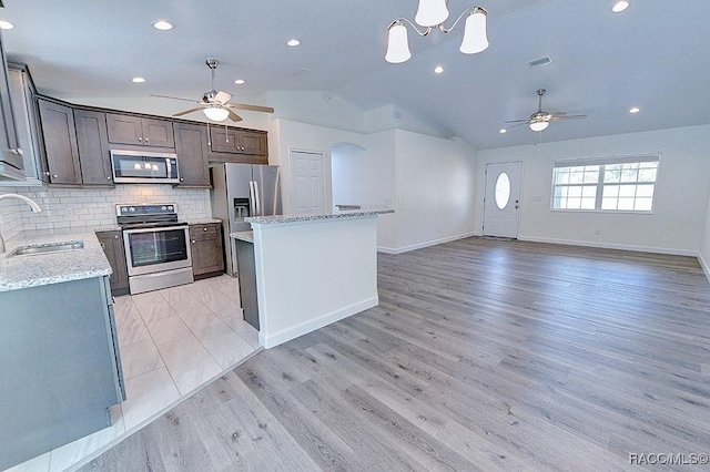 kitchen featuring appliances with stainless steel finishes, sink, decorative backsplash, a center island, and light stone counters