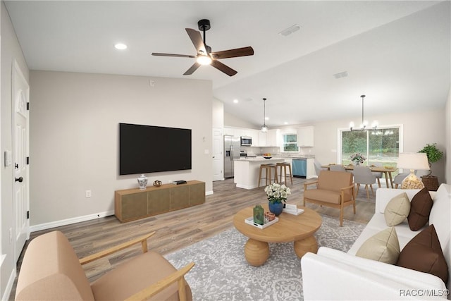 living room with ceiling fan with notable chandelier, wood-type flooring, and lofted ceiling