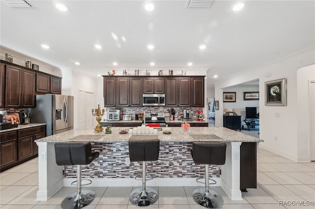 kitchen with a large island, a breakfast bar, stainless steel appliances, and light stone counters