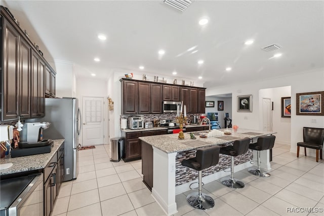 kitchen featuring a kitchen island with sink, light stone countertops, ornamental molding, appliances with stainless steel finishes, and a kitchen bar