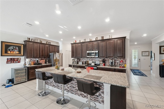 kitchen featuring a kitchen breakfast bar, stainless steel appliances, light tile patterned floors, wine cooler, and an island with sink