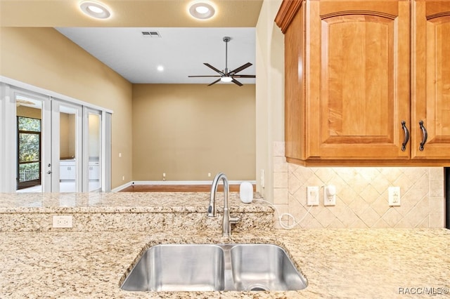 kitchen featuring ceiling fan, sink, light stone counters, and decorative backsplash