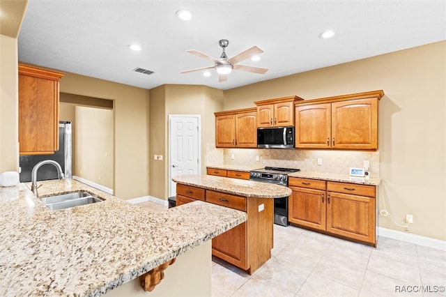 kitchen with sink, appliances with stainless steel finishes, ceiling fan, light stone countertops, and decorative backsplash