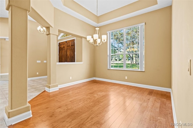 unfurnished room with an inviting chandelier, wood-type flooring, and ornate columns