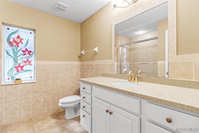 bathroom with tile walls, tile patterned flooring, vanity, toilet, and a textured ceiling