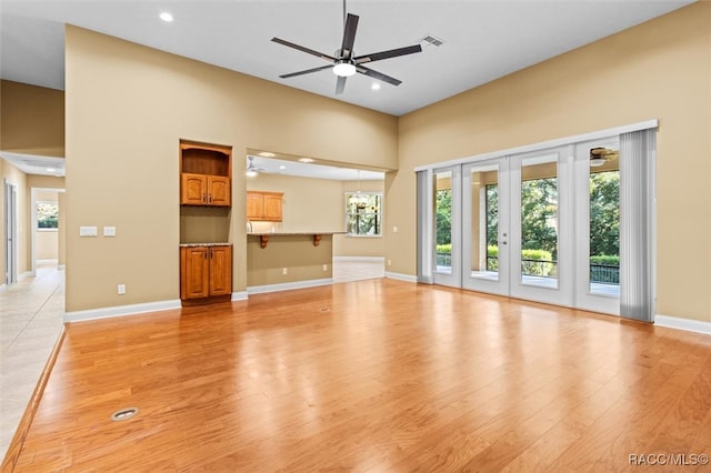 unfurnished living room with a towering ceiling, ceiling fan, and light hardwood / wood-style flooring