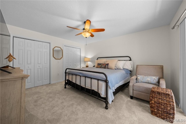 bedroom with two closets, ceiling fan, and light carpet