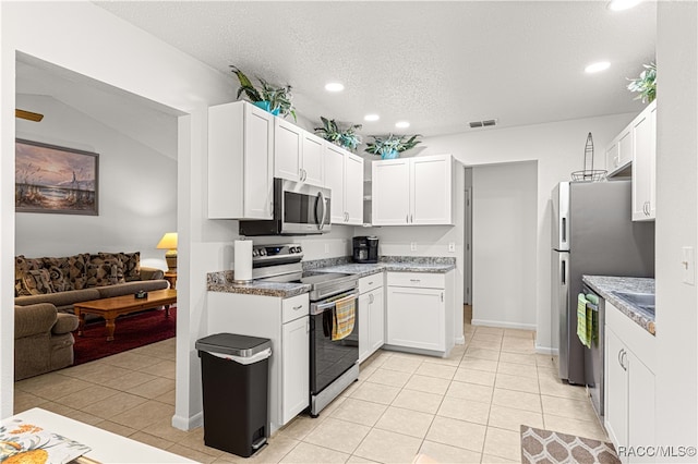 kitchen with lofted ceiling, white cabinets, light tile patterned floors, a textured ceiling, and appliances with stainless steel finishes