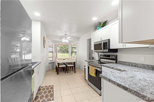 kitchen with appliances with stainless steel finishes, light stone counters, a textured ceiling, white cabinets, and light tile patterned flooring