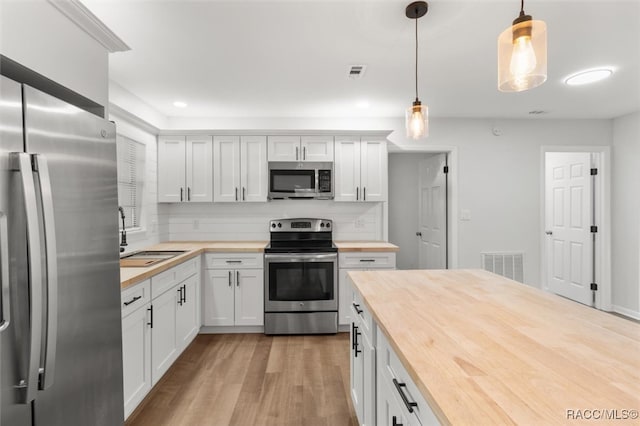 kitchen with white cabinetry, butcher block counters, stainless steel appliances, and hanging light fixtures