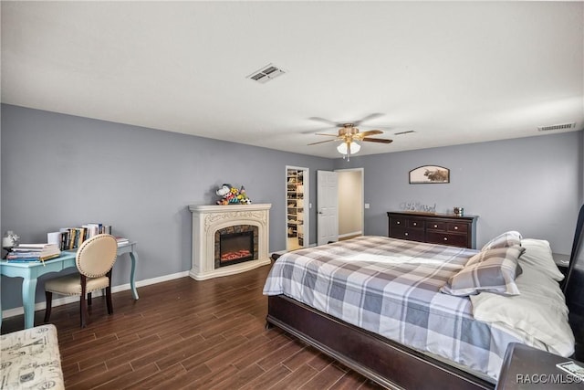 bedroom featuring a warm lit fireplace, wood finished floors, visible vents, and baseboards