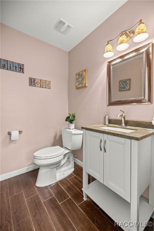 bathroom featuring visible vents, baseboards, toilet, wood tiled floor, and vanity