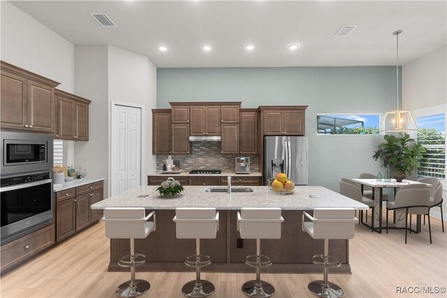 kitchen with light stone counters, an island with sink, appliances with stainless steel finishes, and sink