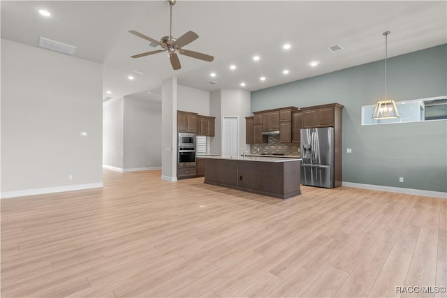 kitchen with tasteful backsplash, decorative light fixtures, light wood-type flooring, and appliances with stainless steel finishes